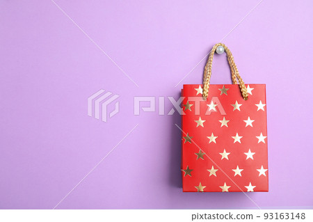 Red shopping paper bag with star pattern on violet background, space for text 93163148