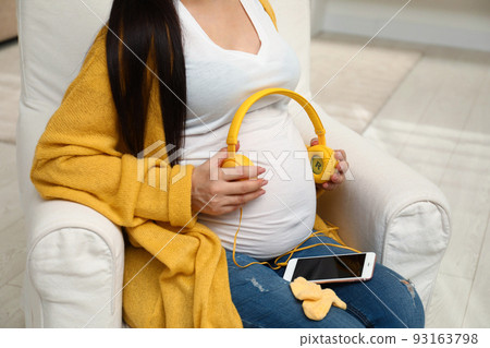 Pregnant woman with headphones and smartphone at home, closeup Pregnant woman with headphones and smartphone at home, closeup 93163798