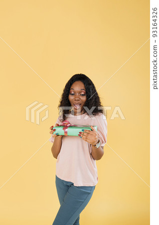 Portrait of african american woman with afro hair, wearing pink t-shirt, posing with gift box 93164326