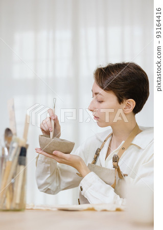 woman ceramist in the workshop makes mugs out of clay. small business or hobby is the creation of ceramic products woman ceramist in the workshop makes mugs out of clay. small business or hobby is the creation of ceramic products 93164416