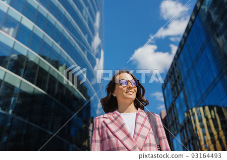 business woman in a pink jacket goes to work in the office and smiles. A successful confident European woman entrepreneur  93164493