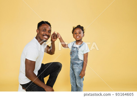 Smiling african dad and his daughter girl in casual clothes posing isolated on yellow background 93164605