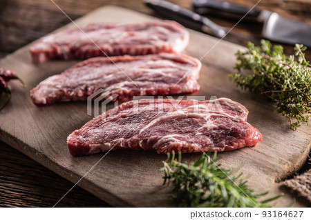 Raw pork neck cut on a cutting board with rosemary and thyme herbs Raw pork neck cut on a cutting board with rosemary and thyme herbs 93164627