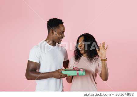 Happy african man giving gifts to his girlfriend, pink studio background, free space. 93164998
