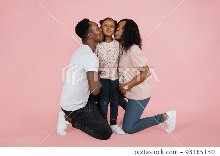 Happy african american woman and her husband kissing their daughter on pink background, Happy african american woman and her husband kissing their daughter on pink background, 93165130