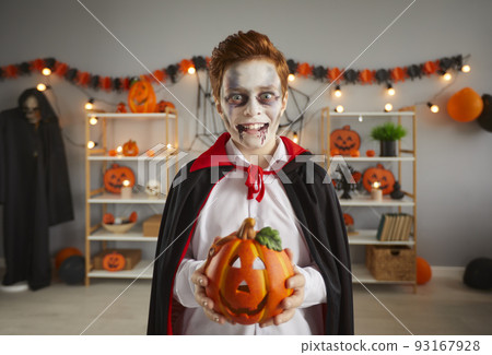 Child dressed up in a spooky Halloween vampire costume holding his jack-o-lantern 93167928
