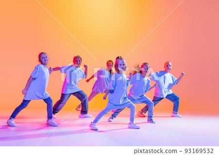 Hip-hop dance, street style. Happy children, little active girls in casual style clothes dancing isolated on orange background in purple neon light. 93169532