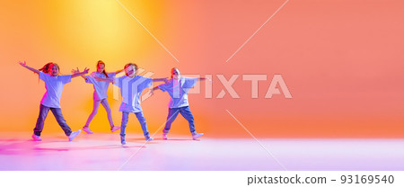 Portrait of cheerful, active little girls, happy kids dancing isolated on orange background in neon light. Concept of music, fashion, art, childhood, hobby 93169540