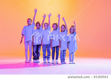 Dance group of happy, active little girls in t-shirts and jeans in action isolated on orange background in neon. Concept of music, fashion, art, childhood Dance group of happy, active little girls in t-shirts and jeans in action isolated on orange background in neon. Concept of music, fashion, art, childhood 93169561