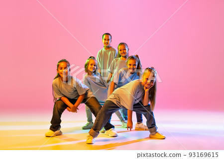 Portrait of cheerful, active little girls, happy kids dancing isolated on orange background in neon light. Concept of music, fashion, art, childhood, hobby Portrait of cheerful, active little girls, happy kids dancing isolated on orange background in neon light. Concept of music, fashion, art, childhood, hobby 93169615