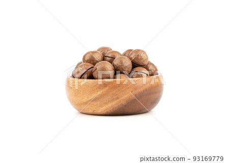 Wooden bowl full of macadamia nuts on a white background. 93169779