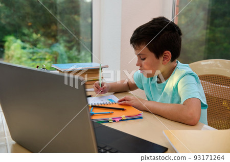 Distance learning, online education. Caucasian happy schoolboy with book studying at home with laptop and doing school homework. Back to school concept with copy advertising space Distance learning, online education. Caucasian happy schoolboy with book studying at home with laptop and doing school homework. Back to school concept with copy advertising space 93171264
