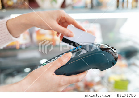 The woman swipes a Bank card through the payment machine to complete the purchase payment. Hands close-up and side view. NFC concept, business and banking operations The woman swipes a Bank card through the payment machine to complete the purchase payment. Hands close-up and side view. NFC concept, business and banking operations 93171799