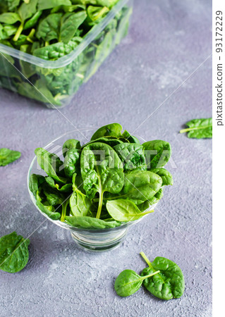 Fresh baby spinach leaves in a glass bowl and behind on a texture table. Vertical view. Close-up Fresh baby spinach leaves in a glass bowl and behind on a texture table. Vertical view. Close-up 93172229
