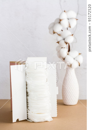 A box with clean disposable sanitary pads and a branch of cotton on the table. Women's health and comfort concept. Vertical view A box with clean disposable sanitary pads and a branch of cotton on the table. Women's health and comfort concept. Vertical view 93172520