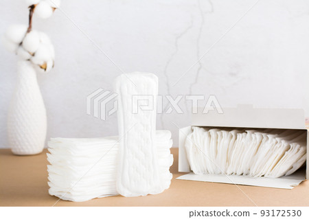 Clean disposable sanitary pads in a stack and in a box and a branch of cotton on a beige background. Women's health and comfort concept. Copy space Clean disposable sanitary pads in a stack and in a box and a branch of cotton on a beige background. Women's health and comfort concept. Copy space 93172530