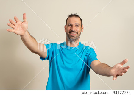 Free hugs for the person who had a bad day. Cheerful friendly latin male model in blue t-shirt, pulling hands towards camera, wanting to hug, smiling broadly, welcoming friend to come into his arms. 93172724