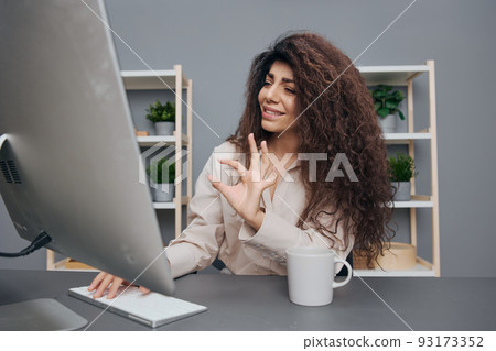 Cheerful tanned adorable curly Latin businesswoman in linen shirt speak in video conference gesture Okay in home office. Copy space. Attractive freelancer work from home using modern desktop computer Cheerful tanned adorable curly Latin businesswoman in linen shirt speak in video conference gesture Okay in home office. Copy space. Attractive freelancer work from home using modern desktop computer 93173352