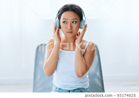 Excited shocked tanned lovely young Asian lady in headphones looks aside listens to external sounds at home interior living room. Sound Studio Stream Social media concept. Cool offer Banner Wide angle 93174028