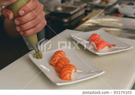 Close up of sushi master prepares sushi for serving in modern commercial kitchen Close up of sushi master prepares sushi for serving in modern commercial kitchen 93174103