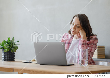 woman in the office is working or looking thoughtfully into the distance. a beautiful European business woman in a pink jacket is sitting at a desk 93174449