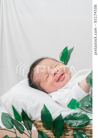 Beautiful newborn baby (4 days old), lying smiling, in bamboo fiber basket and surrounded by green leaves, Healthy medical concept 93174506