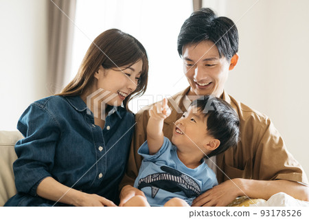 A smiling Japanese family sitting on the sofa / Child-rearing family image A smiling Japanese family sitting on the sofa / Child-rearing family image 93178526