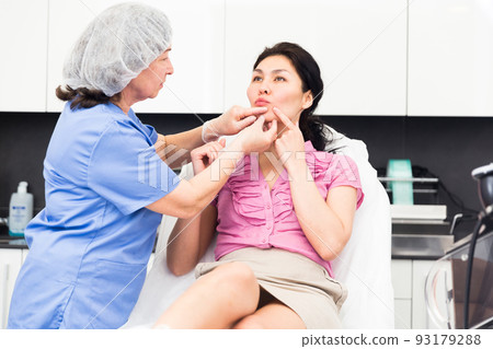 Cosmetologist examining lips of female client before procedure 93179288