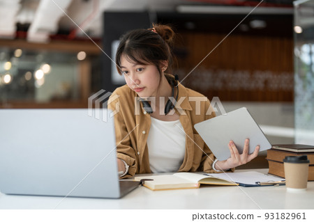 Smiling Asian young female using headset looking at laptop screen listen and learning online courses. Happy business woman with headphones video call for customer service 93182961