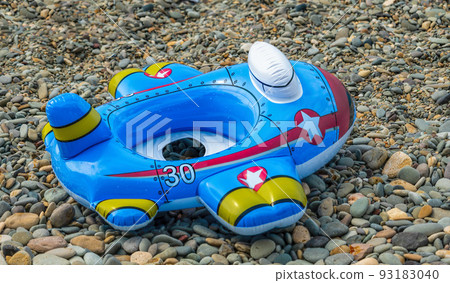 Bright children's inflatable circle lying on the ground on the pebbles beach. Lifebuoy blue in the shape of a airplane 93183040