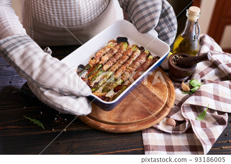 woman holding ceramic baking dish with baked aspargus covered with bacon 93186005