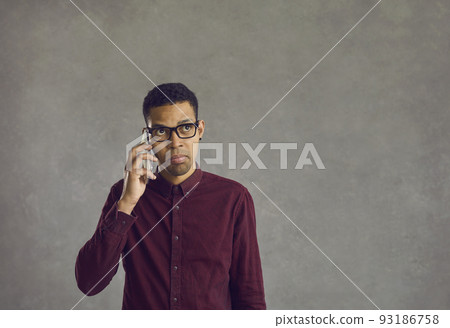 Confused young black man holding mobile phone, making call and waiting for answer 93186758