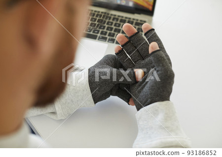 Young man who has rheumatoid arthritis wears compression gloves for relieving pain Young man who has rheumatoid arthritis wears compression gloves for relieving pain 93186852