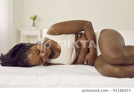Young black woman having menstrual cramps, lying on bed and holding hands on her belly Young black woman having menstrual cramps, lying on bed and holding hands on her belly 93186853
