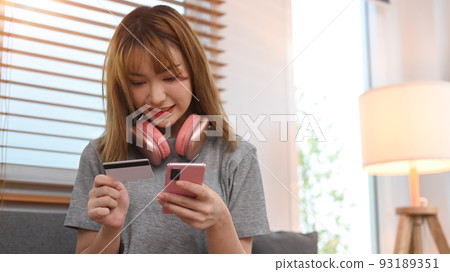 Happy young woman holding credit card and using smart phone. Online shopping, e-commerce concept 93189351