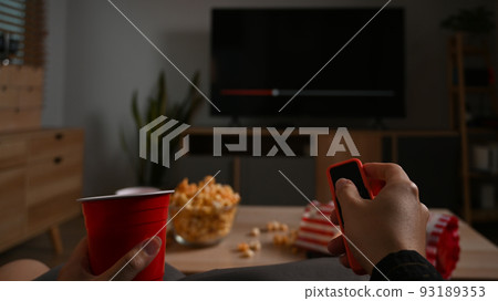 Man hand holding remote control, watching TV at home. Entertainment and leisure activity concept 93189353