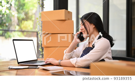 Small business entrepreneur having phone conversation and confirming orders from customer on laptop. Online selling concept 93189355