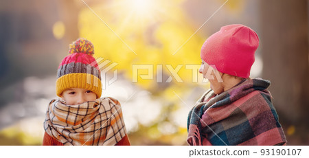 Children in warm hats and scarves standing in autumnal park. 93190107