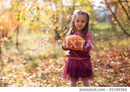 Cute little girl in autumn park with orange color leaves and yellow pumpkin Cute little girl in autumn park with orange color leaves and yellow pumpkin 93190368