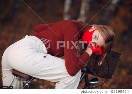 Young woman riding bicycle in red gloves and face mask at autumn park. Young woman riding bicycle in red gloves and face mask at autumn park. 93190454