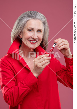Good-looking mature woman in red putting gloss on her lops 93191372