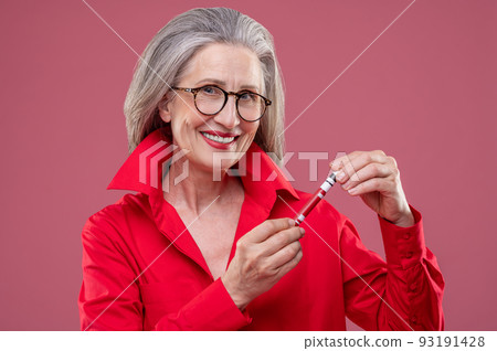 Woman in red bright shirt holding lip gloss and looking contented Woman in red bright shirt holding lip gloss and looking contented 93191428