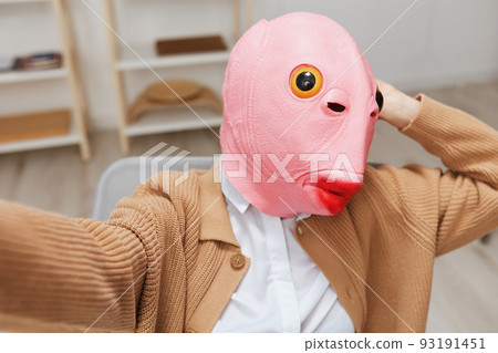 Funny blonde lady in pink fish mask warm sweater doing selfie use phone sitting in armchair at modern home interior. Pause from work, take a break, social media in free time concept. Wide angle Funny blonde lady in pink fish mask warm sweater doing selfie use phone sitting in armchair at modern home interior. Pause from work, take a break, social media in free time concept. Wide angle 93191451