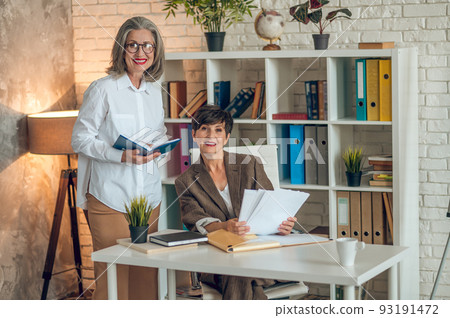 Two businesswomen discussing project details and looking involved Two businesswomen discussing project details and looking involved 93191472