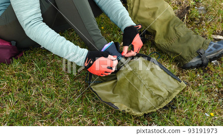 Close-up of a girl hiker's hand in red gloves lacing up her boots. The girl is sitting on the green grass. The concept of mountain tourism. Close-up of a girl hiker's hand in red gloves lacing up her boots. The girl is sitting on the green grass. The concept of mountain tourism. 93191973