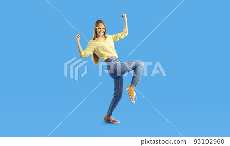 Cheerful successful teen girl rejoices and dances isolated on light blue background. 93192960