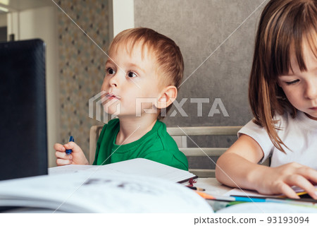 Boy sits at the table, uses a laptop and writes in a notebook 93193094
