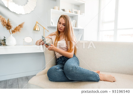 Blonde long-haired woman counting money at home 93196540