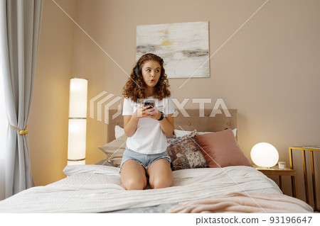 Young happy woman listening music in headphones with smartphone in bed 93196647