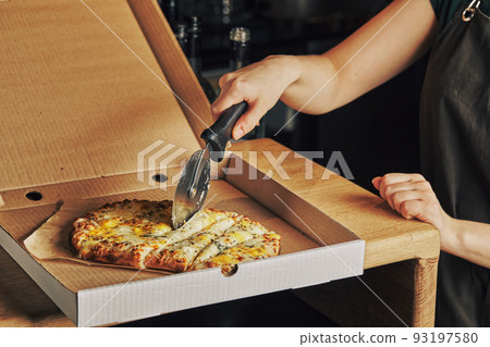 Woman's hand cuts pizza in box with roller knife. Roman square pizza or Pinsa on thick dough, Italian Cuisine Woman's hand cuts pizza in box with roller knife. Roman square pizza or Pinsa on thick dough, Italian Cuisine 93197580